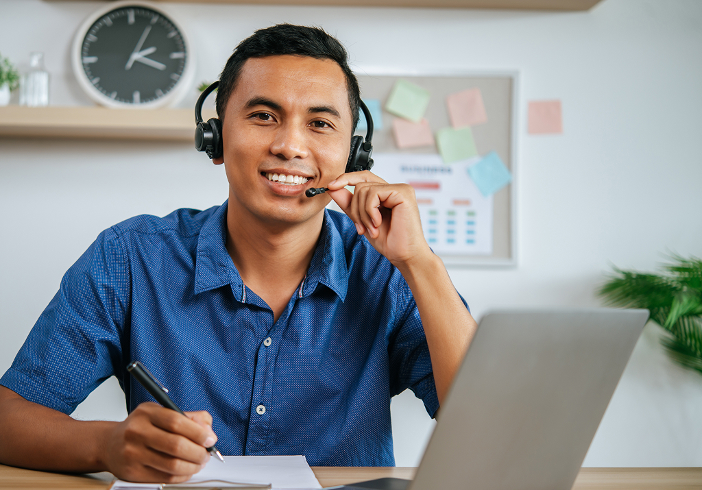 Offshore professional with headphones working on a laptop with documents at their desk